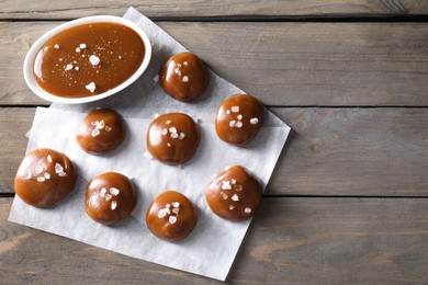 Photo of Tasty candies, caramel sauce and salt on wooden table, top view. Space for text