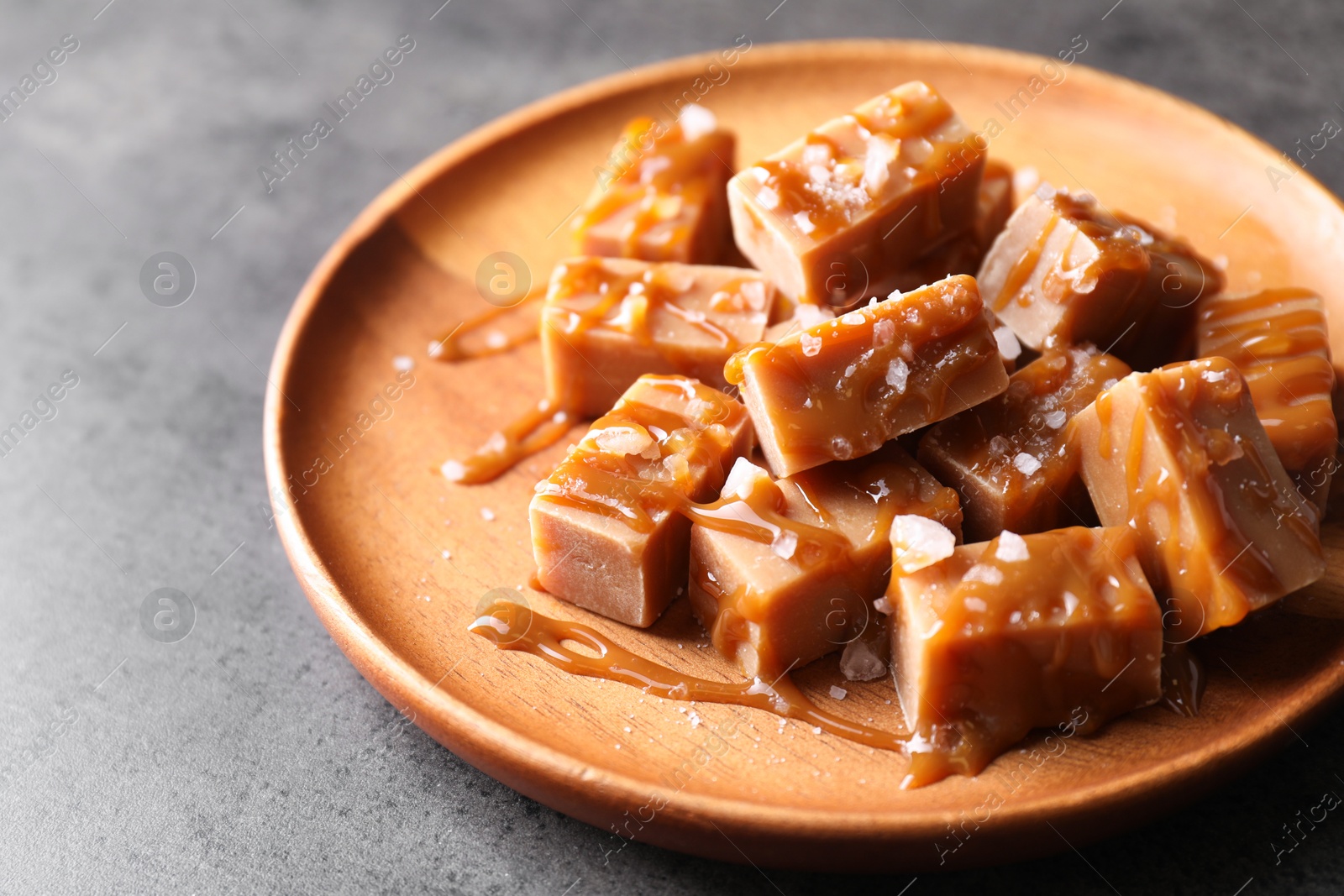 Photo of Plate with tasty candies, caramel sauce and salt on grey table, closeup