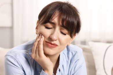 Upset young woman suffering from toothache indoors