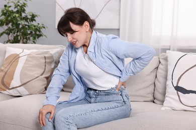 Photo of Upset woman suffering from back pain on sofa at home