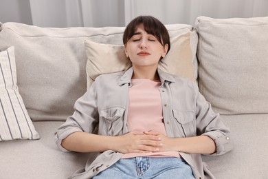 Photo of Upset woman suffering from abdominal pain on sofa at home