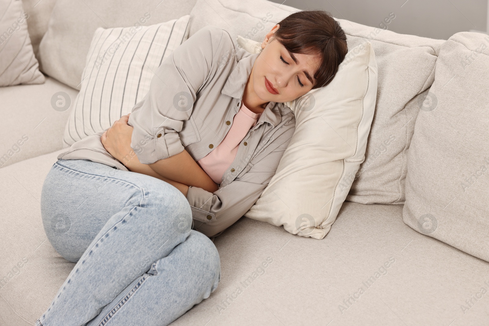 Photo of Upset woman suffering from abdominal pain on sofa at home