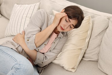 Photo of Upset woman suffering from headache on sofa at home