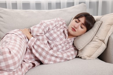 Upset woman suffering from abdominal pain on sofa at home