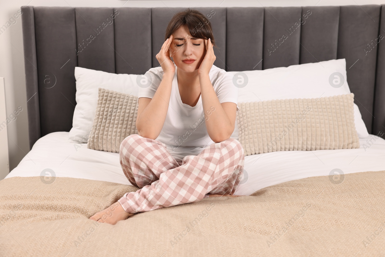 Photo of Upset woman suffering from headache on bed at home