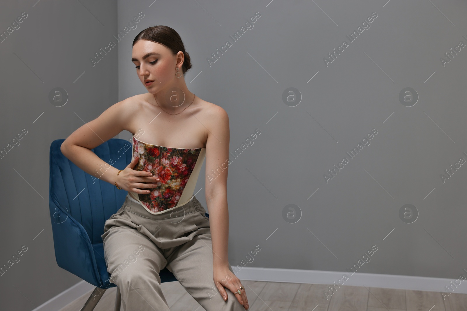 Photo of Beautiful young woman in stylish corset on armchair indoors, space for text