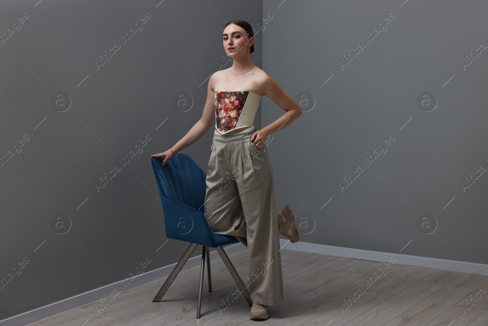 Photo of Beautiful young woman in stylish corset near armchair indoors
