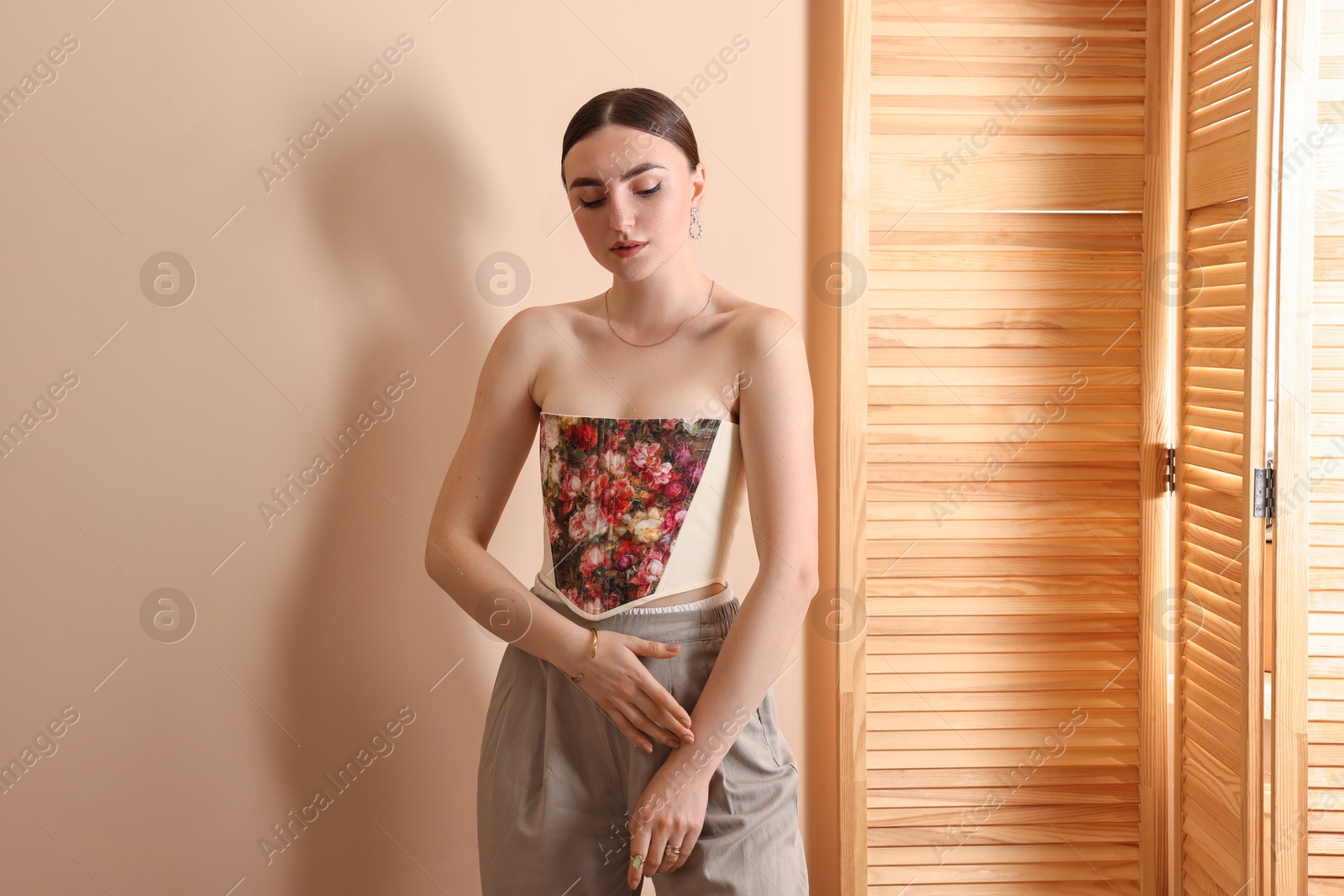 Photo of Beautiful young woman in stylish corset near beige wall
