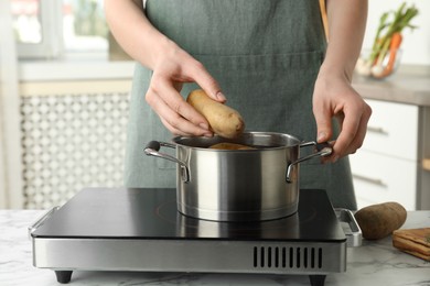 Woman putting potato into metal pot on stove, closeup