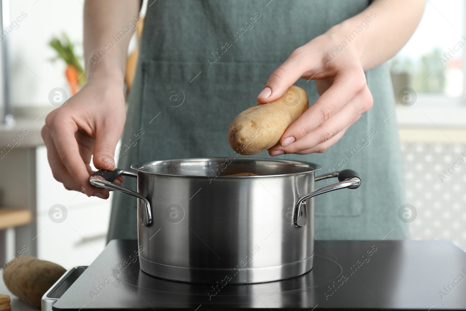 Photo of Woman putting potato into metal pot on stove, closeup