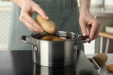 Woman putting potato into metal pot on stove, closeup