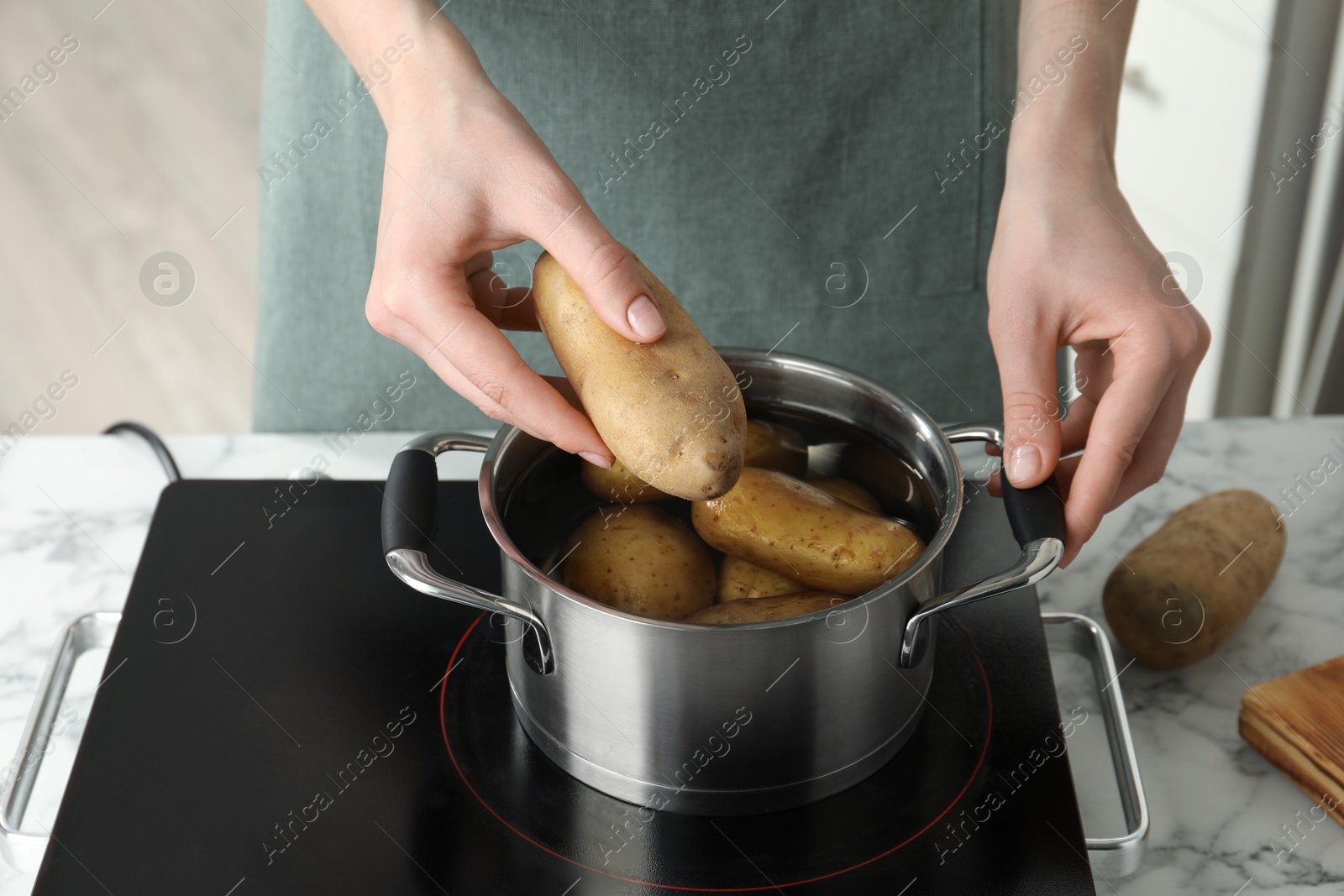 Photo of Woman putting potato into metal pot on stove, closeup