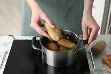 Woman putting potato into metal pot on stove, closeup