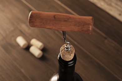 Photo of Wine bottle with corkscrew on wooden table, closeup