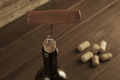 Wine bottle with corkscrew on wooden table, closeup