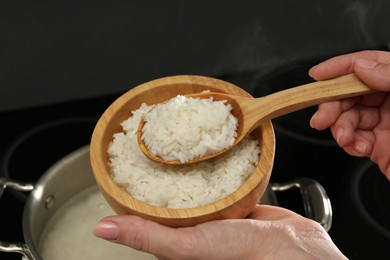 Photo of Woman taking boiled rice from pot into bowl, closeup