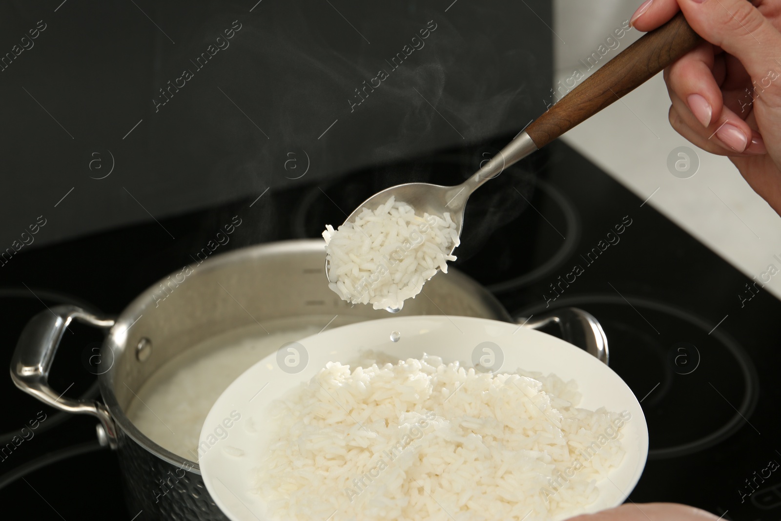 Photo of Woman taking boiled rice from pot into plate, closeup