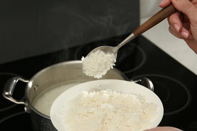 Woman taking boiled rice from pot into plate, closeup