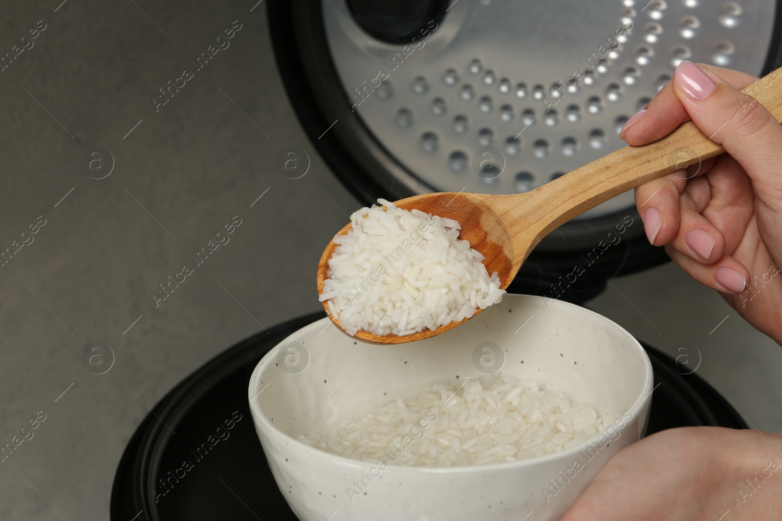 Photo of Woman taking boiled rice into bowl on grey background, closeup