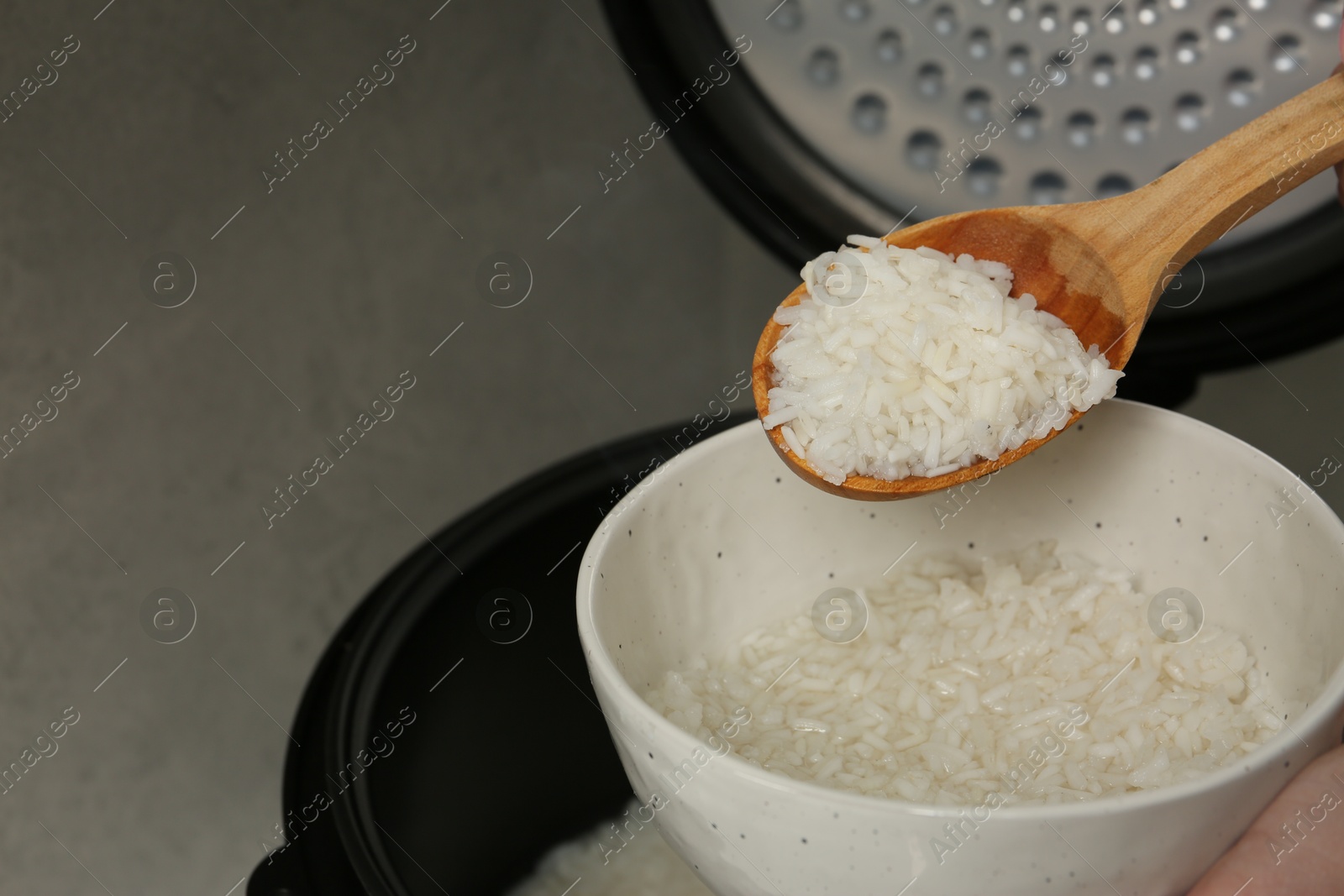 Photo of Woman taking boiled rice into bowl on grey background, closeup. Space for text