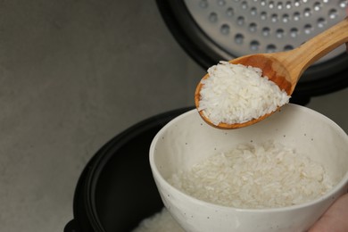 Photo of Woman taking boiled rice into bowl on grey background, closeup. Space for text