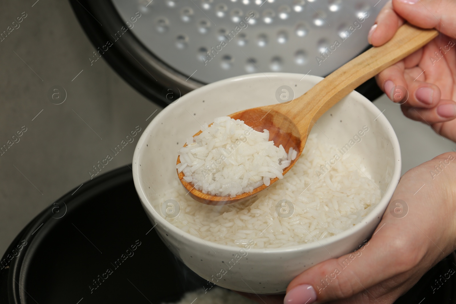 Photo of Woman taking boiled rice into bowl on grey background, closeup