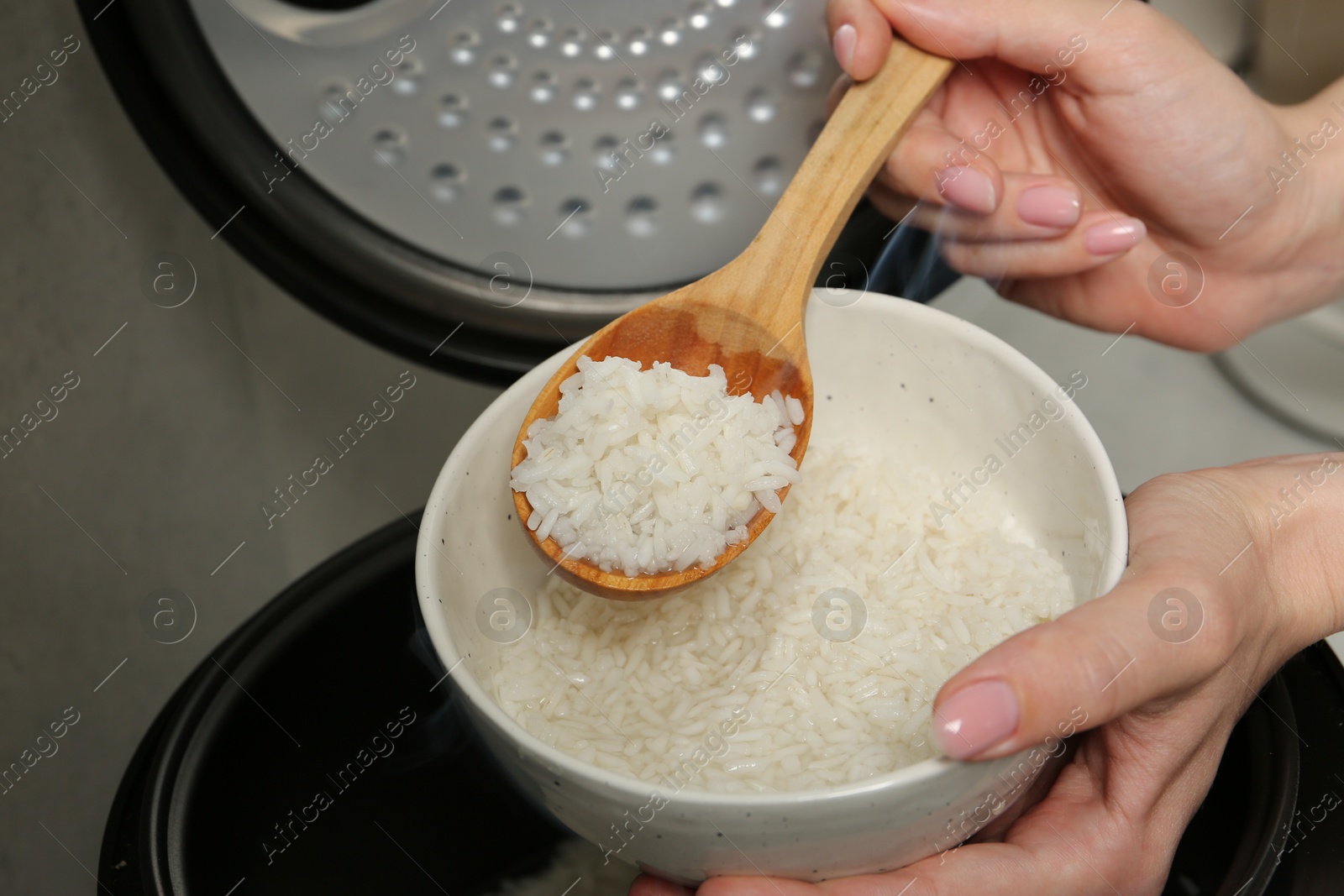 Photo of Woman taking boiled rice into bowl on grey background, closeup