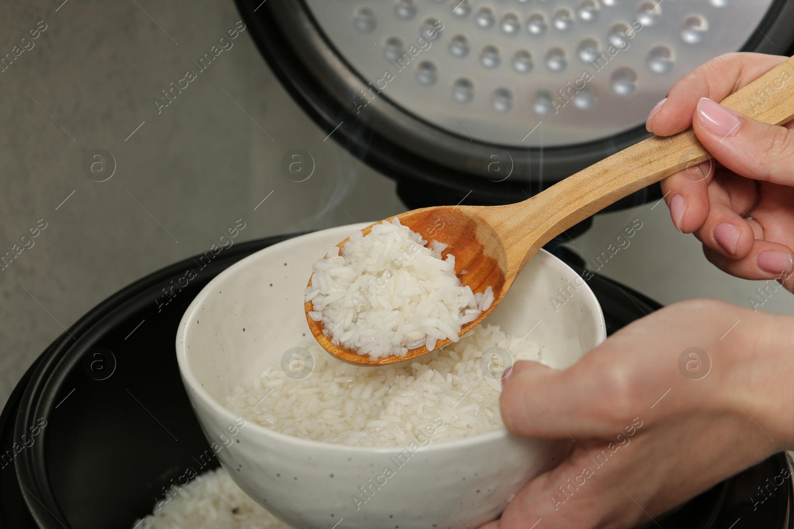 Photo of Woman taking boiled rice into bowl on grey background, closeup