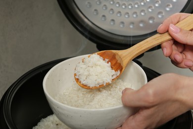 Photo of Woman taking boiled rice into bowl on grey background, closeup