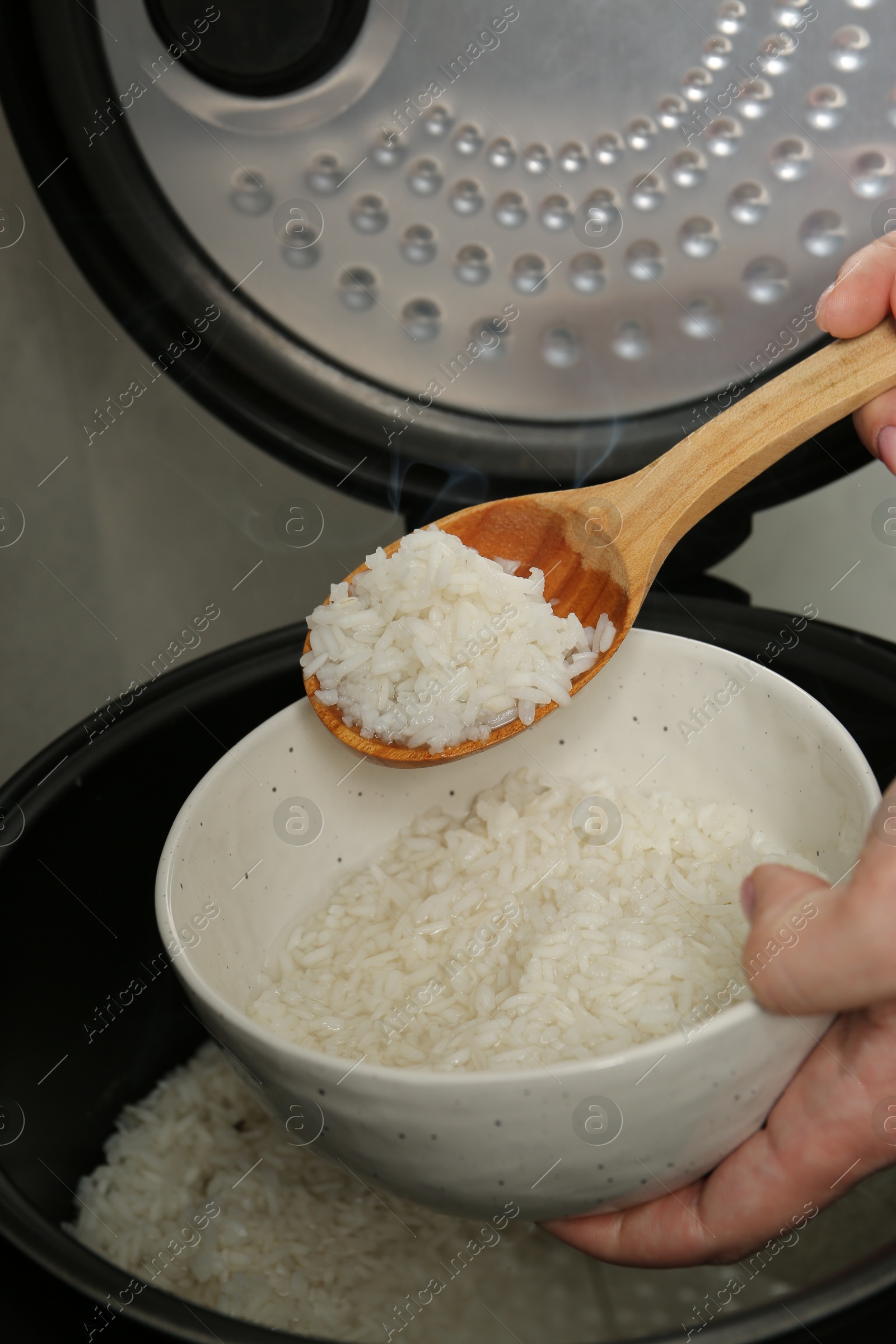 Photo of Woman taking boiled rice into bowl on grey background, closeup