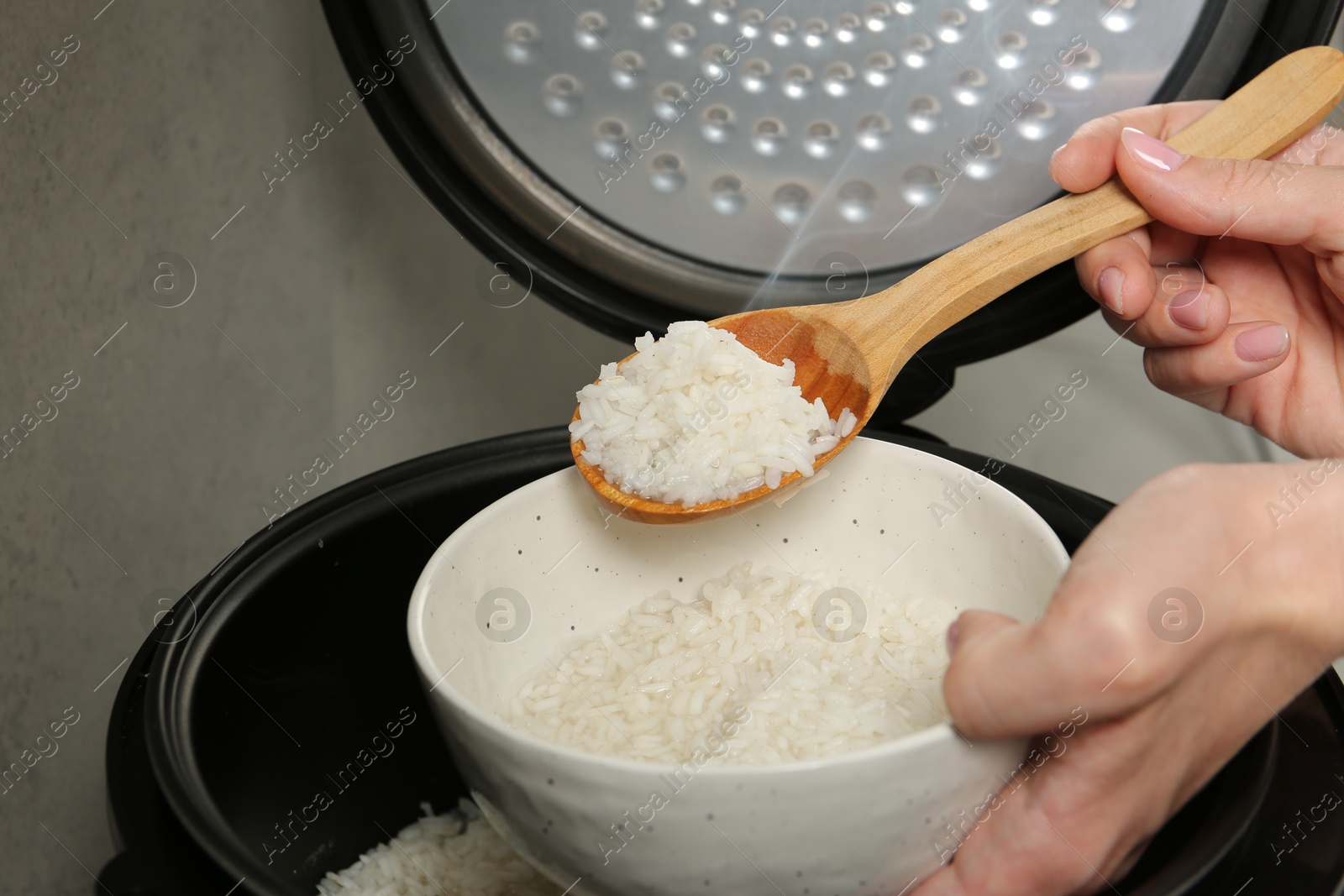 Photo of Woman taking boiled rice into bowl on grey background, closeup