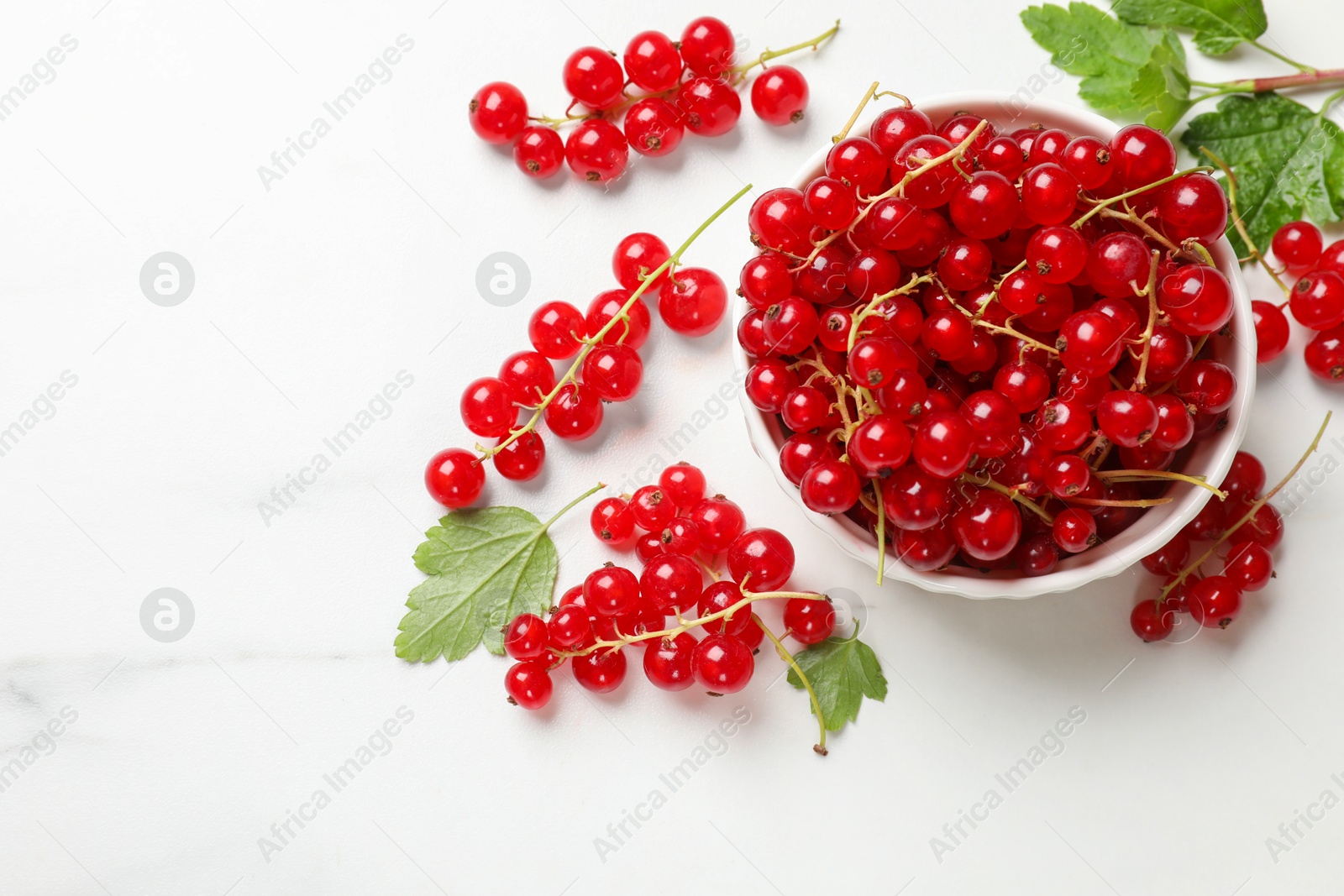 Photo of Fresh red currant berries in bowl on white table, top view. Space for text