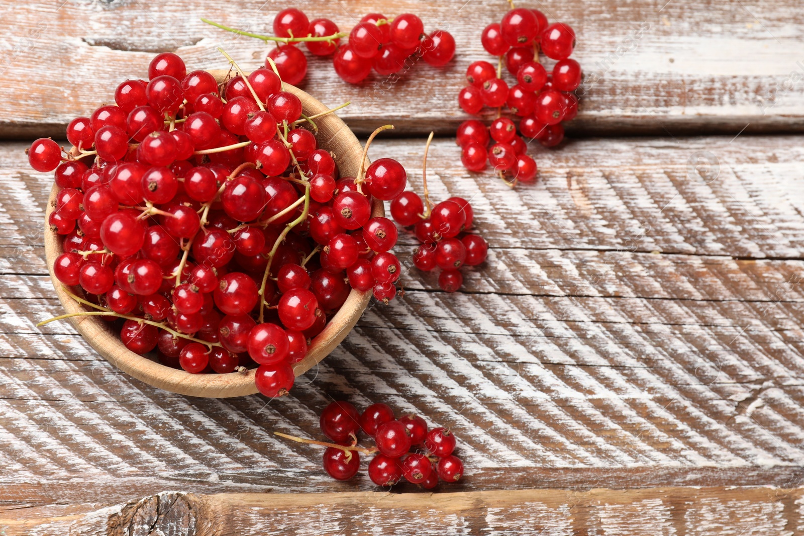 Photo of Fresh red currant berries in bowl on wooden table, top view. Space for text