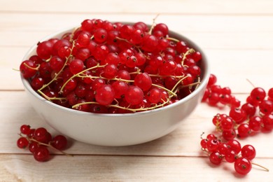 Fresh red currant berries in bowl on white wooden table, closeup