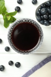 Delicious acai juice in glass, berries and mint on white wooden table, flat lay