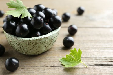 Photo of Fresh ripe black currant berries and leaves on wooden table, closeup