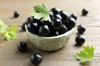 Photo of Fresh ripe black currant berries and leaves on wooden table, closeup