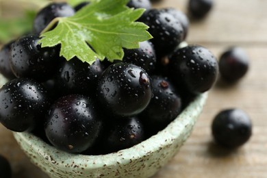 Fresh ripe black currant berries and leaf on wooden table, closeup