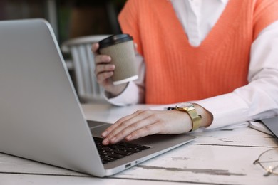 Photo of Female student with laptop and coffee studying at table in cafe, closeup