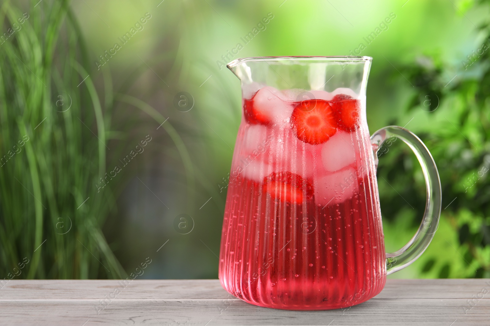 Photo of Freshly made strawberry lemonade in jug on white wooden table outdoors, space for text