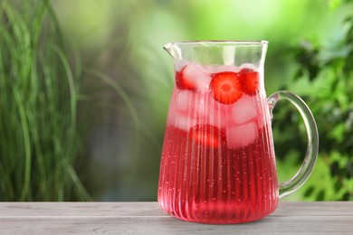 Photo of Freshly made strawberry lemonade in jug on white wooden table outdoors, space for text