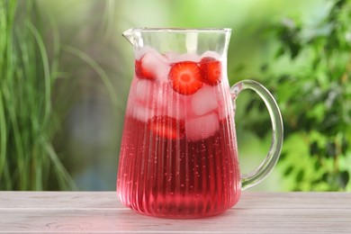 Photo of Freshly made strawberry lemonade in jug on white wooden table outdoors