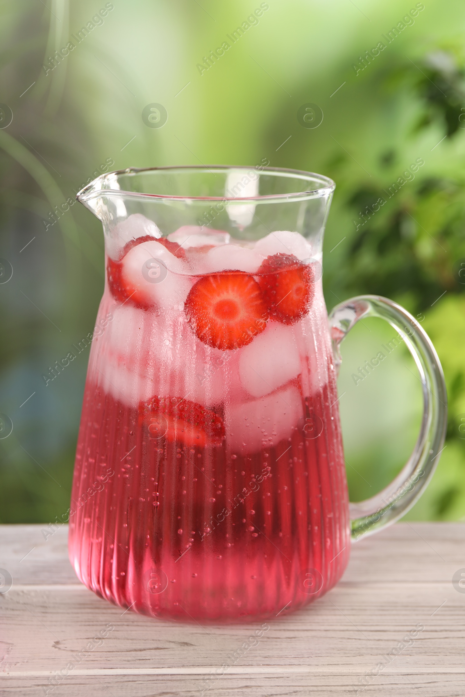 Photo of Freshly made strawberry lemonade in jug on white wooden table outdoors