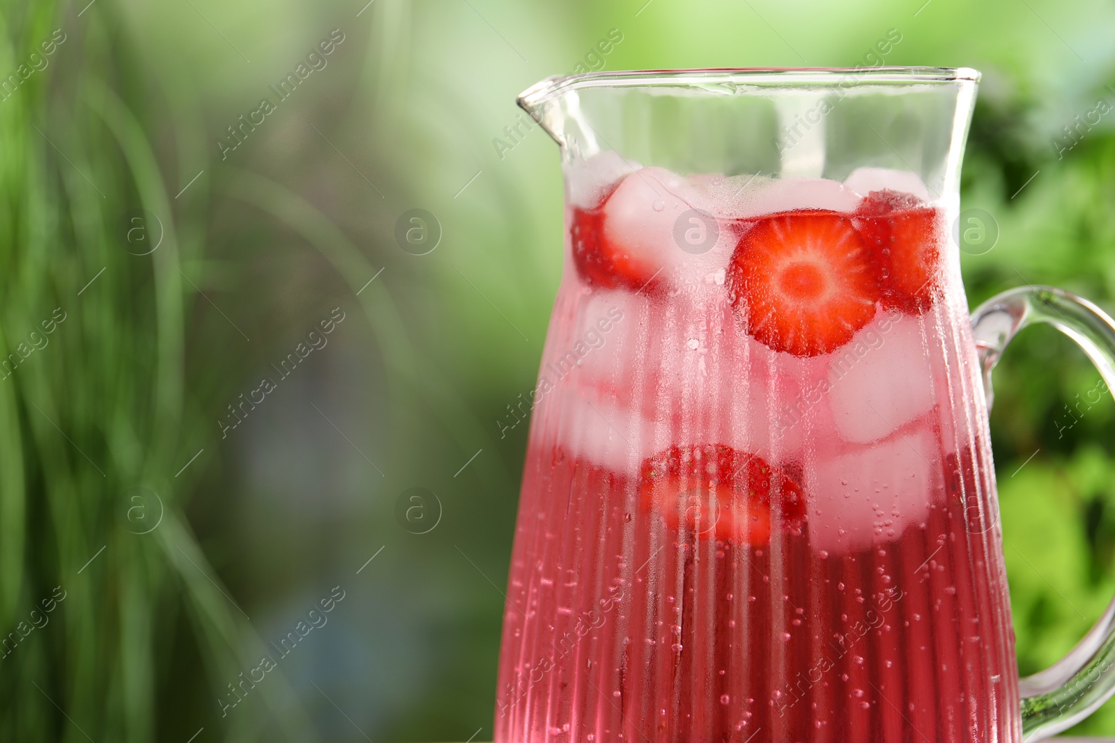 Photo of Freshly made strawberry lemonade in jug outdoors, closeup. Space for text