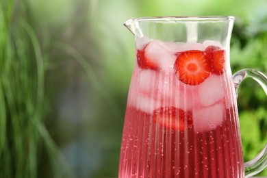 Freshly made strawberry lemonade in jug outdoors, closeup. Space for text