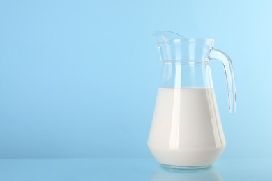Photo of Glass jug of fresh milk on light blue background, space for text