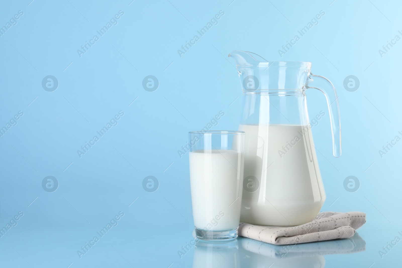 Photo of Jug and glass of fresh milk on light blue background, space for text