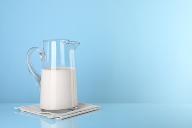 Photo of Glass jug of fresh milk on light blue background, space for text