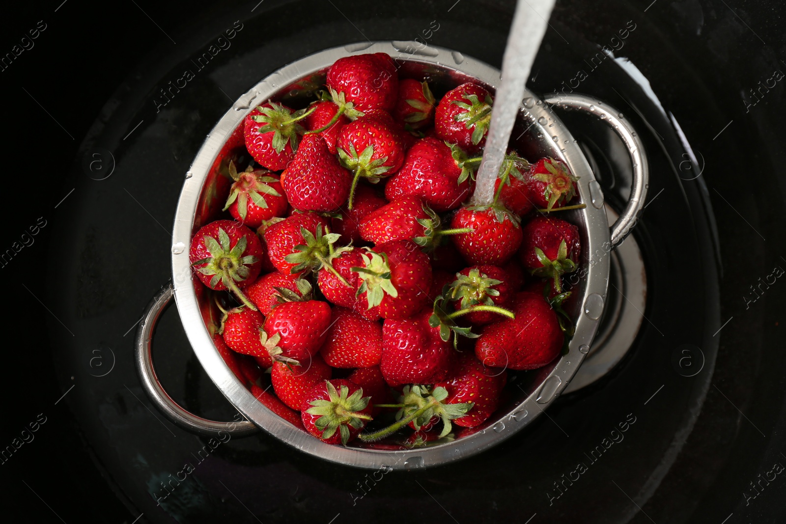 Photo of Washing fresh strawberries under tap water in metal colander in sink, top view