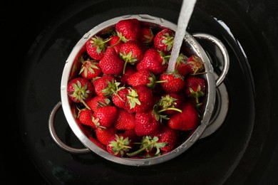 Photo of Washing fresh strawberries under tap water in metal colander in sink, top view